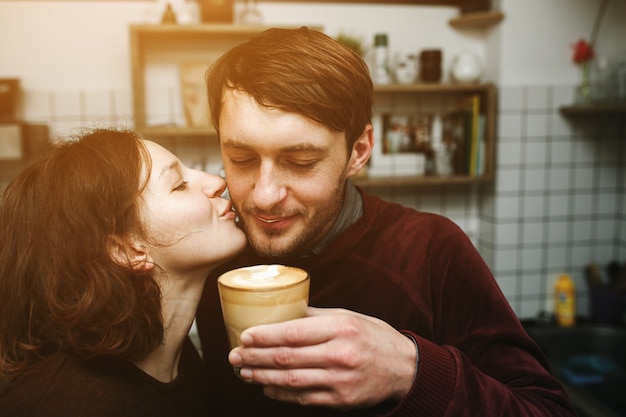 Frau küsst ihren Freund, während Kaffee zu trinken