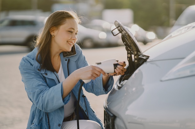 Frau lädt Elektroautos an der elektrischen Tankstelle