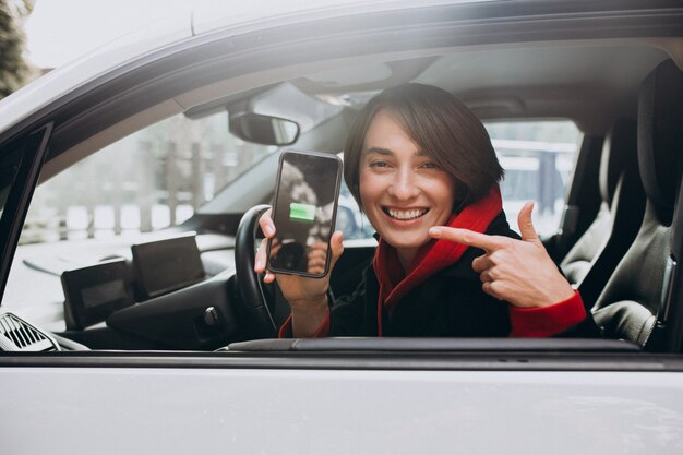 Frau lädt ihr Auto auf und schaut auf den Cherger am Telefon