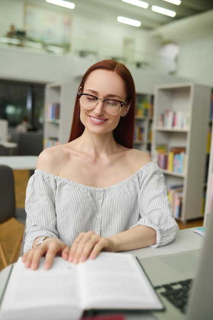 Frau liest ein Buch, das in der Bibliothek sitzt