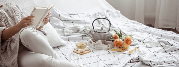 Frau liest ein Buch im Bett mit Tee und Strauß Tulpen