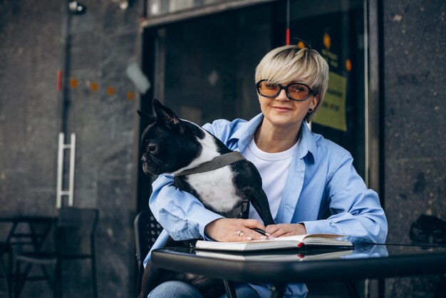 Frau liest ein Buch in einem Café mit ihrer französischen Bulldogge