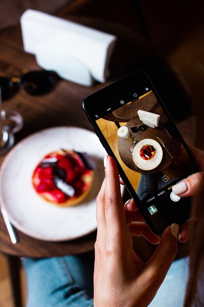 Frau macht Foto von ihrem Dessert mit Smartphone