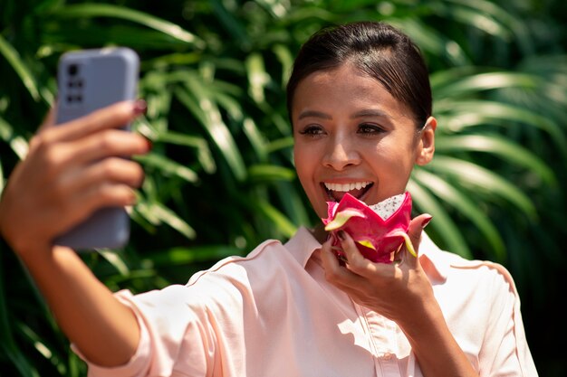 Frau macht Selfie mit Smartphone, während sie Drachenfrucht isst