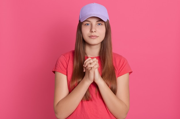 Frau meditiert, die beide ihre Handflächen verbindet, schaut in die Kamera und trägt ein lässiges T-Shirt und eine Baseballkappe