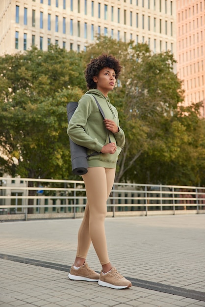 Kostenloses Foto frau mit afro-haar, gekleidet in hoodie-leggings und turnschuhen, hat regelmäßiges fitness-training im städtischen umfeld, um sich im freien fit zu halten