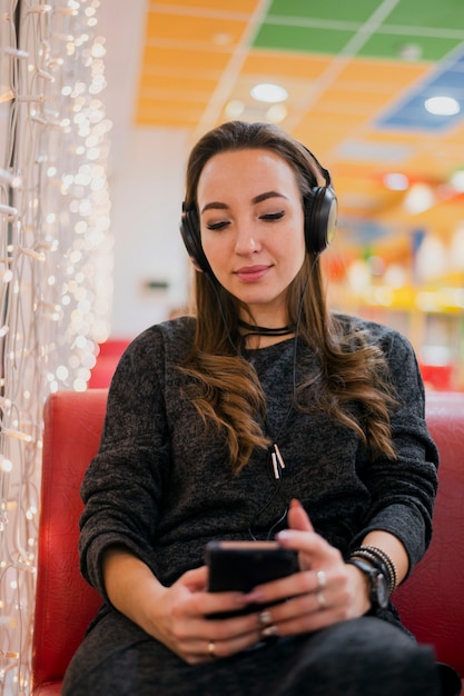 Frau mit Augen schloss die tragenden Kopfhörer, die Telefon nahe Weihnachtslichtern betrachten