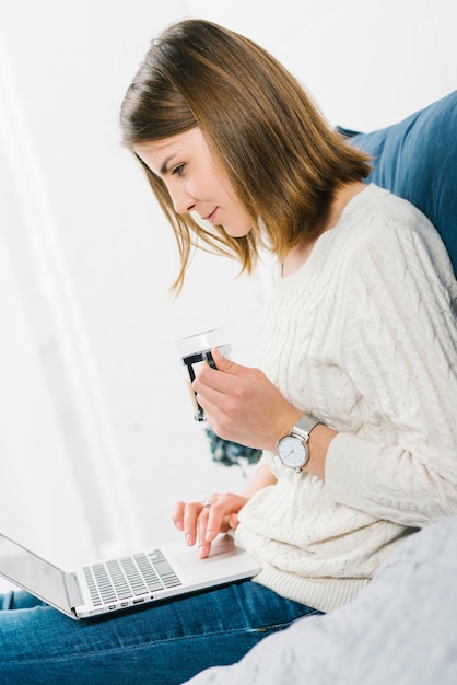 Frau mit Becher unter Verwendung des Laptops auf Bett