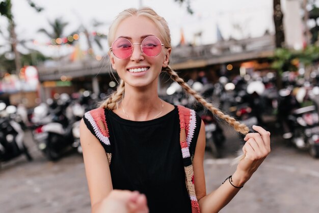 Frau mit blonden Zöpfen, die Spaß im Freien haben und lachen. glückliche Dame trägt modische Sommerkleidung.