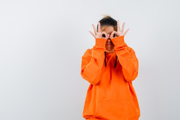 Frau mit Brillengeste in orangefarbenem Hoodie und neugierigem Blick