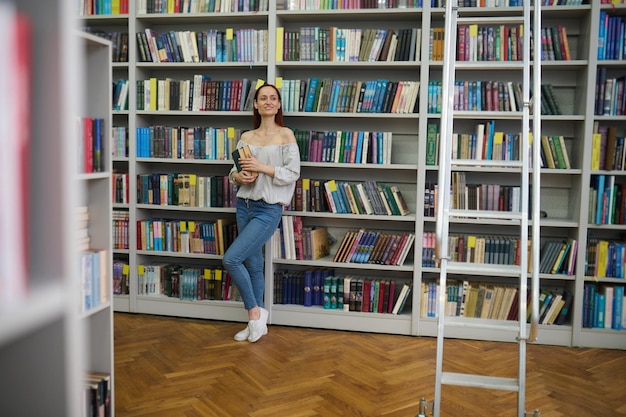 Frau mit Büchern, die in der Bibliothek zur Seite schauen