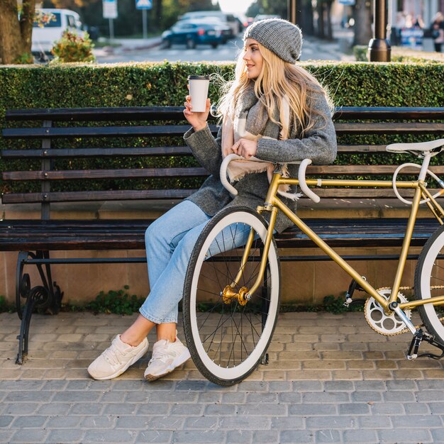 Frau mit Cup und Fahrrad auf Bank