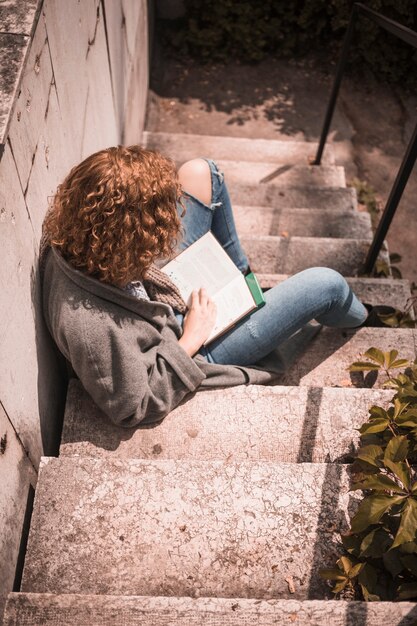 Frau mit dem Buch, das auf Steintreppe sitzt