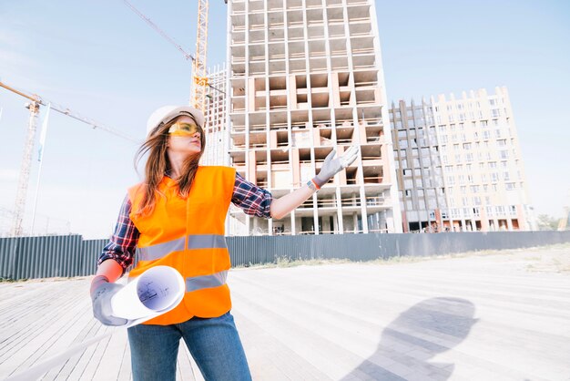 Frau mit dem Entwurf, der auf Baustelle gestikuliert