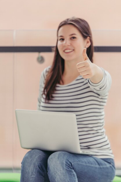 Frau mit dem Laptop, der sich Daumen zeigt