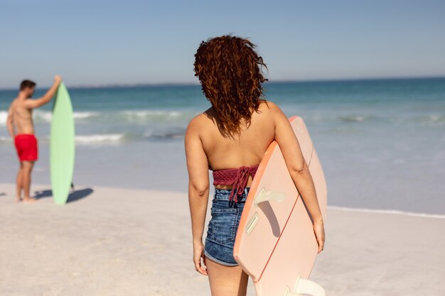 Frau mit dem Surfbrett, das auf Strand im Sonnenschein steht