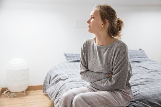 Frau mit den Händen auf dem Magen, der unter den Schmerz leiden, beiseite schauend