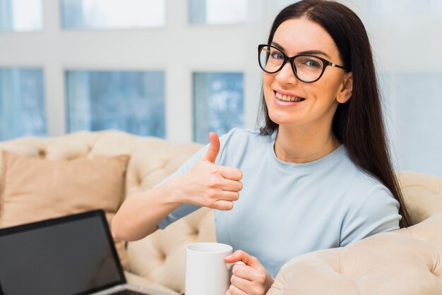 Frau mit der Kaffeetasse, die sich Daumen zeigt