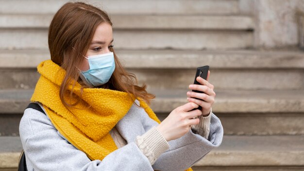 Frau mit der medizinischen Maske, die Bilder mit Smartphone macht