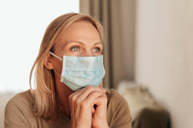 Frau mit der medizinischen Maske, die zu Hause während der Quarantäne reflektiert