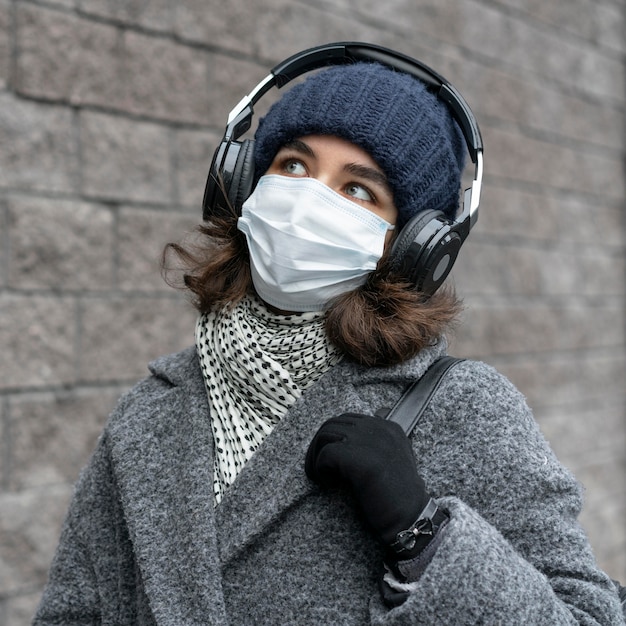 Frau mit der medizinischen Maske in der Stadt, die Musik hört