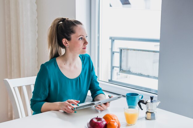 Frau mit der Tablette, die heraus Fenster schaut