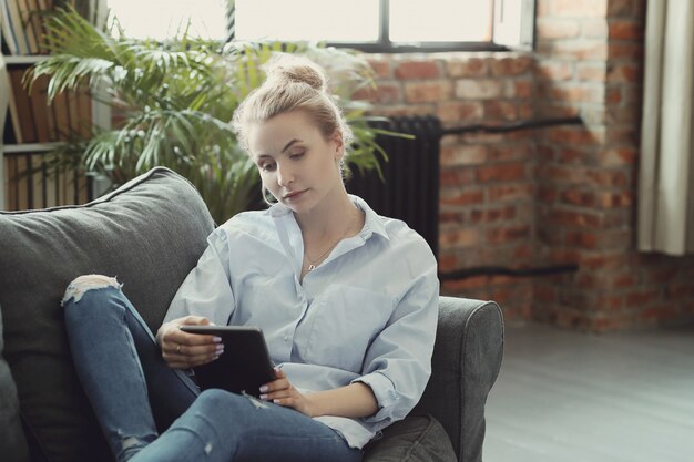 Frau mit digitaler Tablette, auf dem Sofa liegend