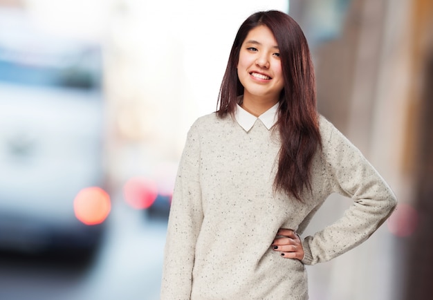 Frau mit einem beige Pullover lächelnd und Hand auf der Hüfte