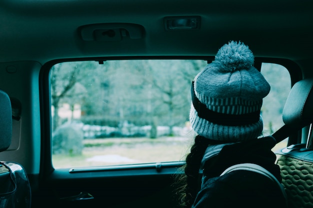 Frau mit einem Hut, der in einem Auto sitzt, das aus dem Fenster schaut