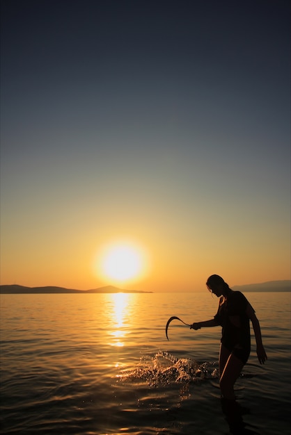 Frau mit einer Sichel am Strand bei Sonnenuntergang