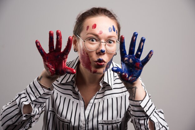 Frau mit Farben auf ihrem Gesicht und Brille auf grauem Hintergrund