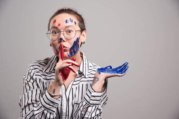 Frau mit Farben im Gesicht und Brille auf Grau