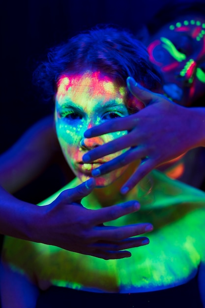 Frau mit fluoreszierendem Make-up mit den Händen auf ihrem Gesicht