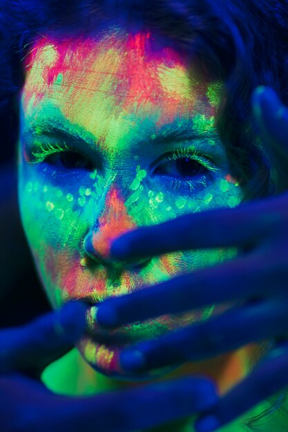 Frau mit fluoreszierendem Make-up und Hand auf ihrem Gesicht