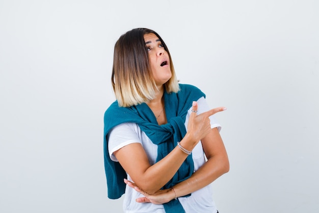 Frau mit gebundenem Pullover, der nach rechts zeigt, im weißen T-Shirt aufschaut und verwundert aussieht. Vorderansicht.