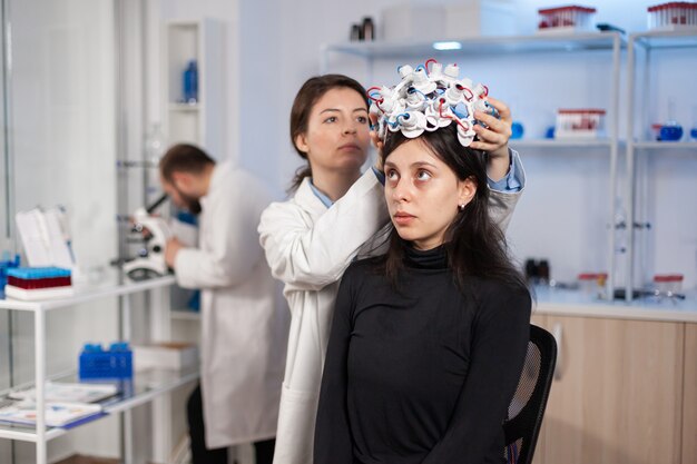 Frau mit Gehirnwellen-Headset im Labor für moderne Medizin mit Neurologe-Arzt-Gesundheitsarzt. Mediziner der Neurowissenschaften, der dem Patienten Sensoren anlegt. Heilung für Krankheiten finden.