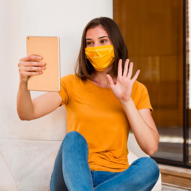 Frau mit gelber Maske, die an Tablette winkt