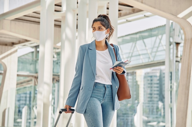 Frau mit Gepäck und medizinischer Maske am Flughafen während der Pandemie