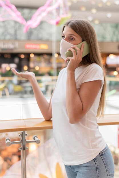 Frau mit Gesichtsmaske, die am Telefon im Einkaufszentrum spricht