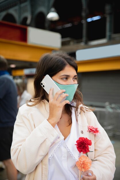Frau mit Gesichtsmaske, die am Telefon spricht, während Blumen hält