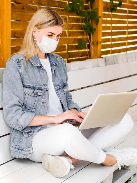 Frau mit Gesichtsmaske, die auf Laptop im Freien arbeitet