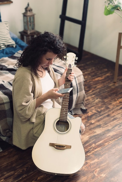 Frau mit Gitarre und Smartphone im Schlafzimmer