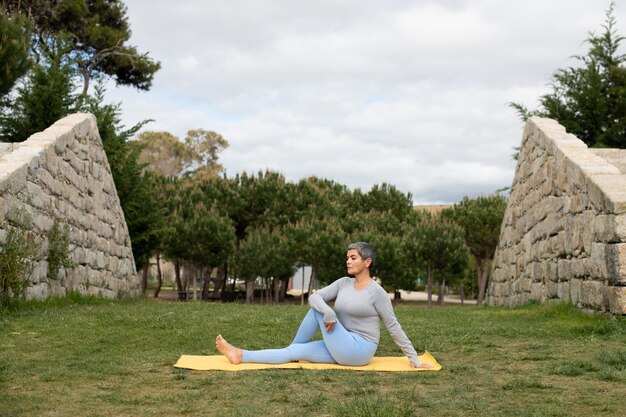 Frau mit grauem Haar beim Yoga im Park. Weibliches Modell in sportlicher Kleidung, die an bewölkten Tagen auf der Matte trainiert. Sport, Hobby, Gesundheitskonzept