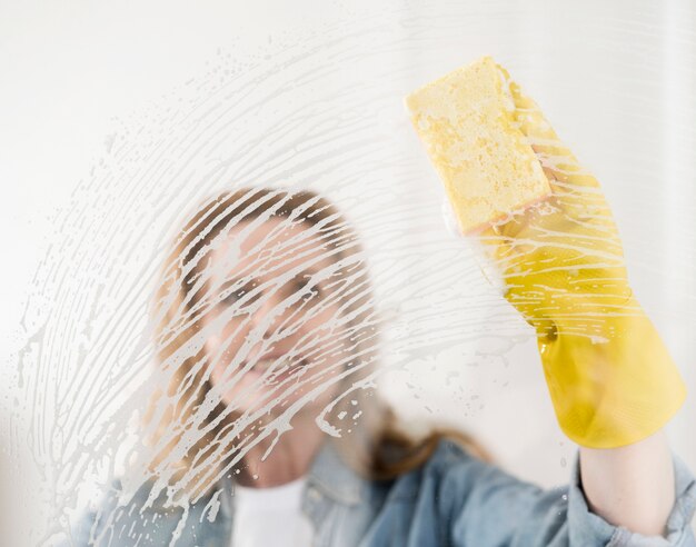 Frau mit Gummihandschuh-Reinigungsfenster mit Schwamm
