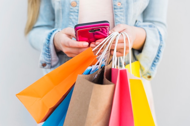 Frau mit hellen Einkaufstüten mit Smartphone