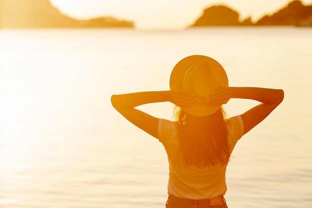 Kostenloses Foto frau mit hut bei sonnenuntergang am ufer eines sees