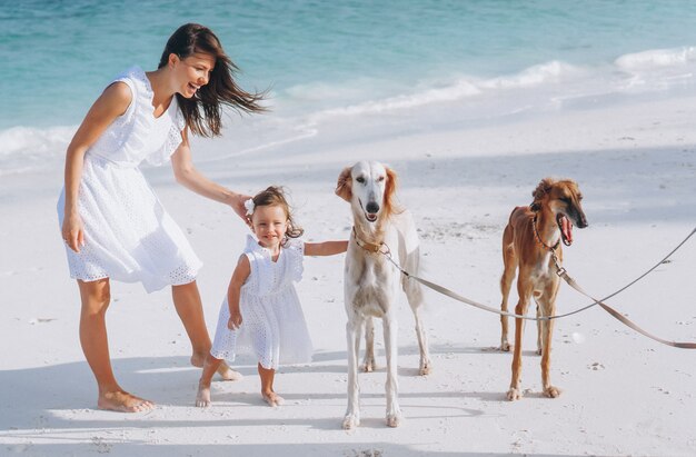 Frau mit ihrer kleinen Tochter, die mit Hunden am Strand durch den Ozean spielt