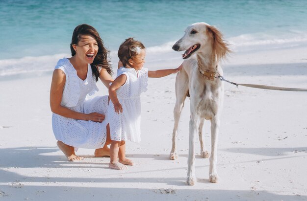 Frau mit ihrer kleinen Tochter, die mit Hunden am Strand durch den Ozean spielt
