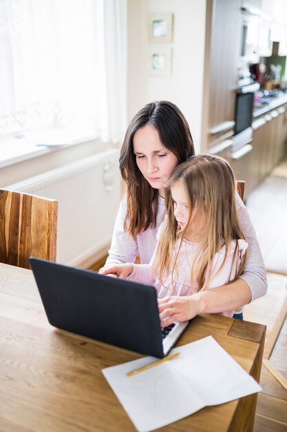 Frau mit ihrer Tochter, die zu Hause an Laptop arbeitet