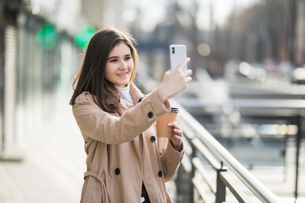 Frau mit Kaffee zum Mitnehmen, der ein Selfie mit Smartphone draußen nimmt